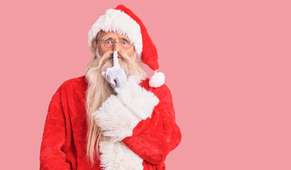 Old senior man with grey hair and long beard wearing traditional santa claus costume asking to be quiet with finger on lips. silence and secret concept.