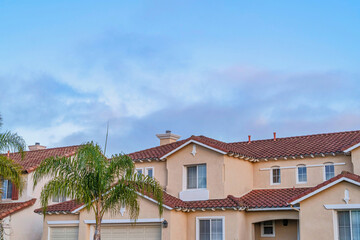 Fototapeta na wymiar Houses with red tile roofs and beige wall against cloudy sky in San Diego CA