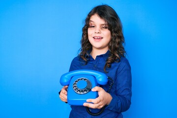 Cute hispanic boy with long hair holding vintage telephone winking looking at the camera with sexy...