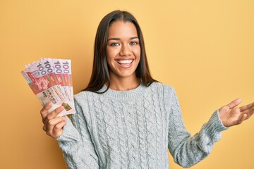 Beautiful hispanic woman holding 100 hong kong dollars banknotes celebrating achievement with happy smile and winner expression with raised hand