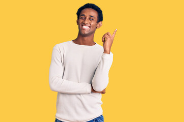 African handsome man wearing casual winter sweater with a big smile on face, pointing with hand and finger to the side looking at the camera.