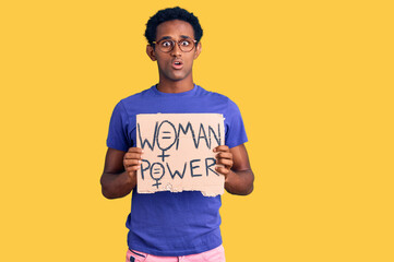 African handsome man holding woman power banner scared and amazed with open mouth for surprise, disbelief face