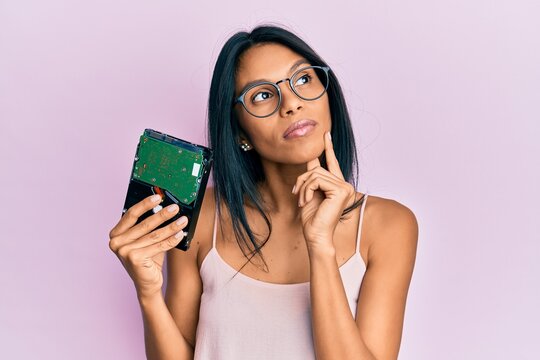 Young african american woman holding hard disk serious face thinking about question with hand on chin, thoughtful about confusing idea