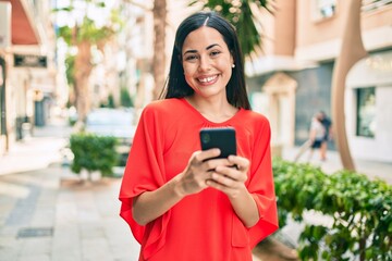 Young latin girl smiling happy using smartphone at the city.