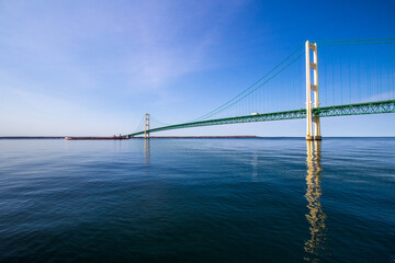Mackinaw Bridge Panorama. Mackinaw Bridge on a sunny day reflected in the clear blue water of Lake Michigan with a Great Lakes freighter at the horizon.