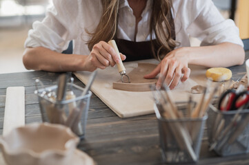 Female potters hand making clay pottery at the table with a different wooden tools close up.
