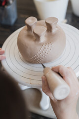Female hands holding stick and making ornament on decorative product. Clay master moulding clay on a pottery and ceramics workshop.