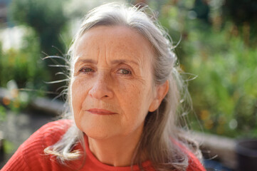 Close up face of happy senior woman with grey hair looking at camera while spending time outdoors during sunny day