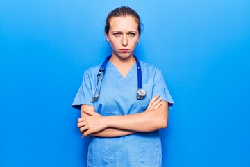 Young blonde woman wearing doctor uniform and stethoscope skeptic and nervous, disapproving expression on face with crossed arms. negative person.