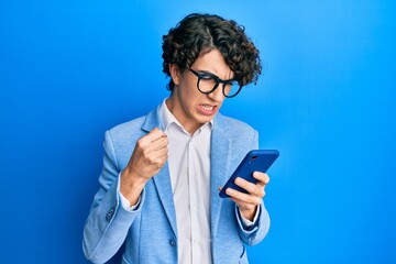 Hispanic young man using smartphone wearing business jacket annoyed and frustrated shouting with...