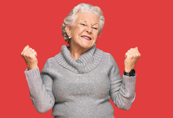 Senior grey-haired woman wearing casual winter sweater very happy and excited doing winner gesture with arms raised, smiling and screaming for success. celebration concept.