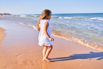 Fototapeta na wymiar Adorable blonde child on back view wearing summer dress playing on the sand at the beach