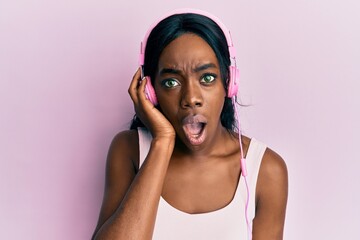 Young african american woman listening to music using headphones scared and amazed with open mouth for surprise, disbelief face