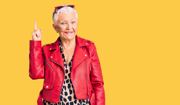 Senior beautiful woman with blue eyes and grey hair wearing a modern style with a red leather jacket pointing finger up with successful idea. exited and happy. number one.