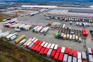 Logistics park with loading hub. Semi-trailer trucks stand on the parking lot and wait for load and unload goods at warehouse ramps. Aerial view at sunset