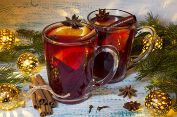 Hot mulled wine with orange, anise and cinnamon on the background of Christmas tree branches and garland. Warming Christmas drink. Festive mood.