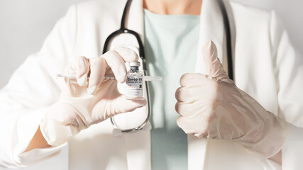 A female doctor in white gown with stethoscope recommended safe and effective Covid-19 Vaccine vial. Authorized, Collaborating, Hope, Partners, Pandemic, Global Vaccine Action Plan, COVAX, Thumbs up.