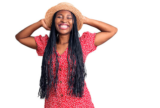Young african american woman wearing summer hat relaxing and stretching, arms and hands behind head and neck smiling happy