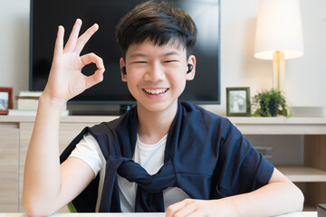 Web cam video call picture of an  asian teenager boy's face cheerful smiling and do Okay Hand sign...