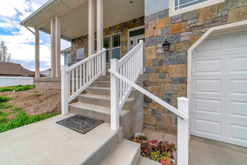 Stairs going up to open porch of home with white garage door against stone wall