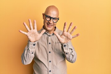 Middle age bald man wearing casual clothes and glasses showing and pointing up with fingers number ten while smiling confident and happy.
