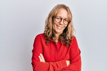 Middle age blonde woman wearing casual clothes and glasses happy face smiling with crossed arms looking at the camera. positive person.