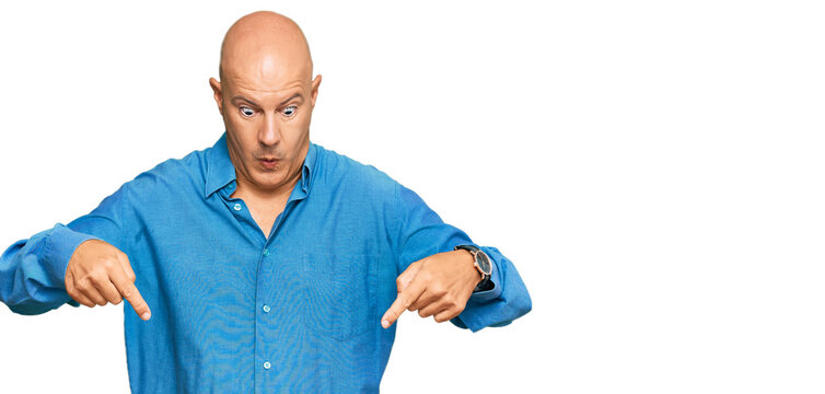 Middle age bald man wearing casual clothes pointing down with fingers showing advertisement, surprised face and open mouth