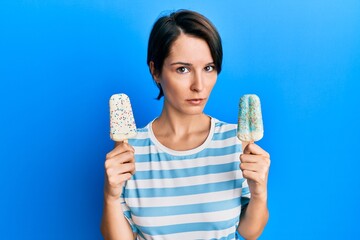 Young brunette woman with short hair holding two ice cream clueless and confused expression. doubt...