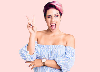 Obraz premium Young beautiful woman with pink hair wearing casual clothes smiling with happy face winking at the camera doing victory sign with fingers. number two.