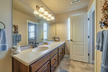 Vanity unit with single oval sink on white countertop over brown wood cabinets