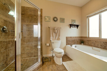 Naklejka na ściany i meble Shower stall toilet and built in bathtub inside bathroom with warm toned tiles