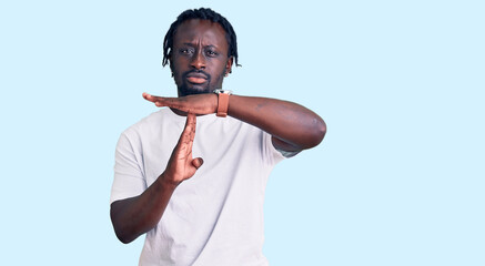Young african american man with braids wearing casual white tshirt doing time out gesture with...