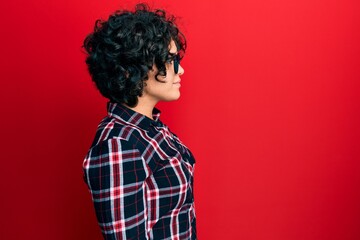 Fototapeta na wymiar Young hispanic woman with curly hair wearing casual clothes and glasses looking to side, relax profile pose with natural face with confident smile.