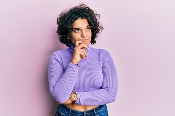 Young hispanic woman with curly hair wearing turtleneck sweater thinking concentrated about doubt...