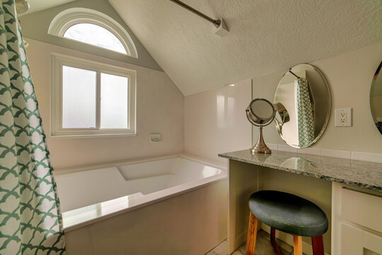 Marble vanity unit with stool and oval mirror beside built in bathroom bathtub