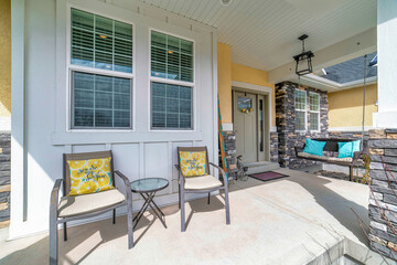 Swing bench and chairs at the open porch of a home viewed on a sunny day