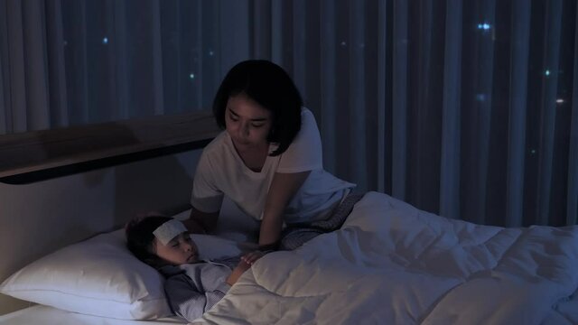 Asian family Mother caring for sick daughter lying in bed with Antipyretic gel sheet on the forehead. Medical and child health concept in night shots.