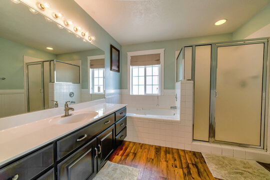 Bathtub and shower stall inside bathroom withw ahite wall and wood floor