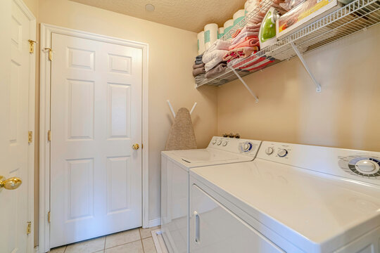 Appliances And Storage Shelf Against White Wall Of A Residential Laundry Room