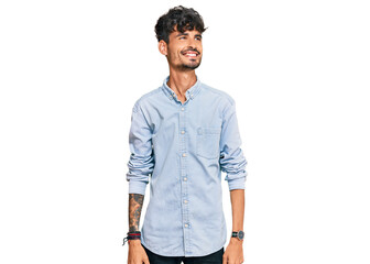 Fototapeta premium Young hispanic man wearing casual clothes looking away to side with smile on face, natural expression. laughing confident.