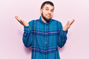 Young handsome man wearing casual shirt clueless and confused with open arms, no idea and doubtful...