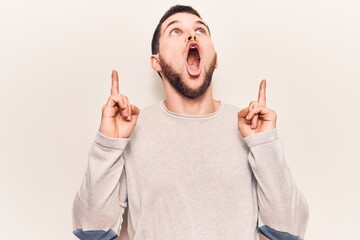 Young handsome man wearing casual sweater amazed and surprised looking up and pointing with fingers and raised arms.