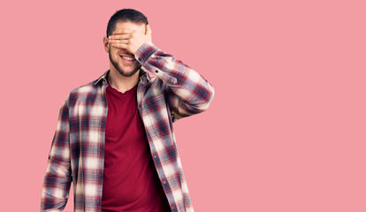 Young handsome man wearing casual shirt smiling and laughing with hand on face covering eyes for surprise. blind concept.