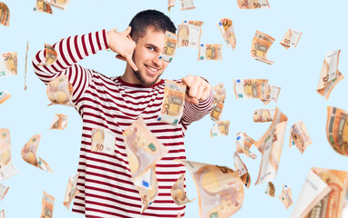 Young handsome man wearing striped sweater smiling doing talking on the telephone gesture and...