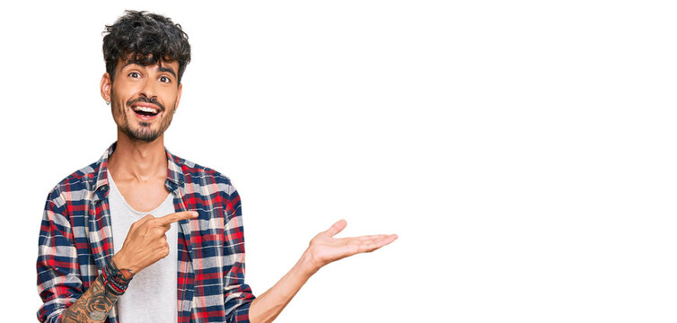 Young hispanic man wearing casual clothes amazed and smiling to the camera while presenting with hand and pointing with finger.