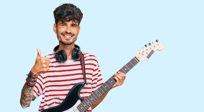 Young hispanic man playing electric guitar smiling happy and positive, thumb up doing excellent and approval sign