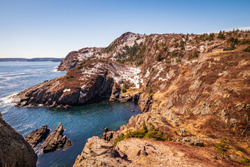 Fototapeta na wymiar A rugged mountain coastline on a sunny day in Spring. The cold Atlantic ocean and the sky are deep blues. The hills and mountains are mostly rocky with some greenery. The cliffs are a red texture.