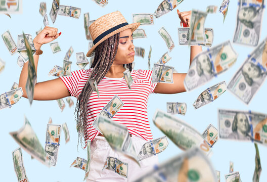Young african american woman with braids wearing summer hat showing arms muscles smiling proud. fitness concept.