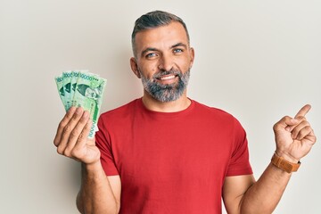 Middle age handsome man holding 10000 south korean won banknotes smiling happy pointing with hand and finger to the side