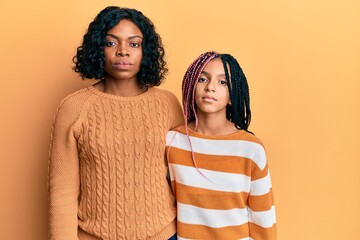 Beautiful african american mother and daughter wearing wool winter sweater relaxed with serious expression on face. simple and natural looking at the camera.
